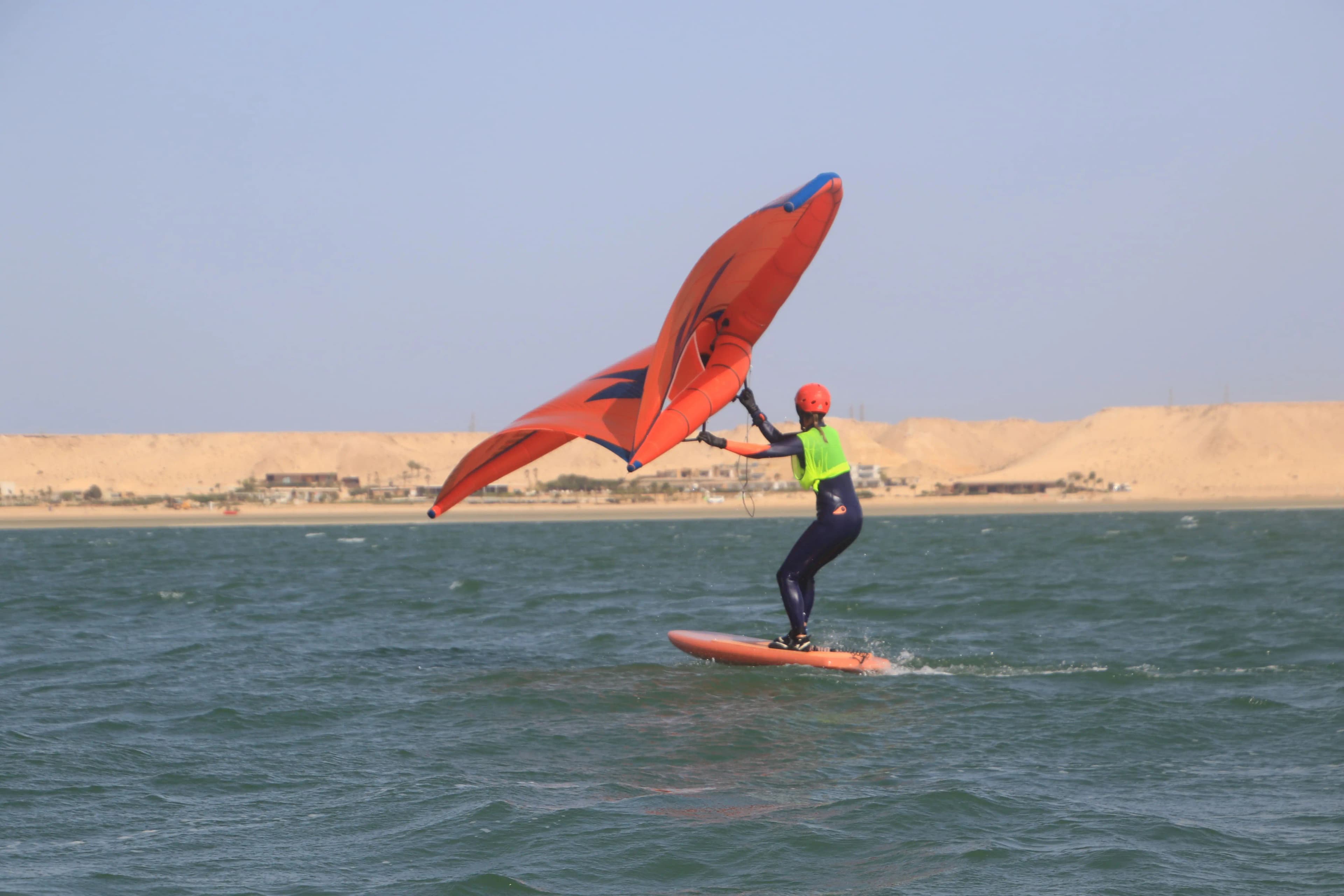 Élève effectuant son premier décollage sur le foil avec une aile orange sur le lagon de Dakhla